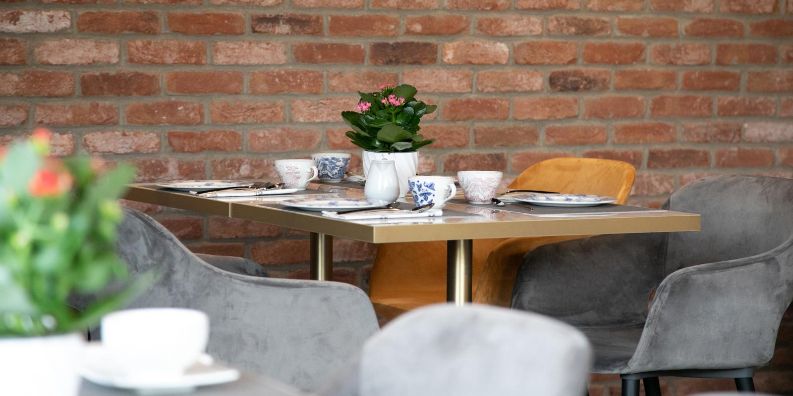 A cozy table setting with colorful cups and potted plants against a brick wall.