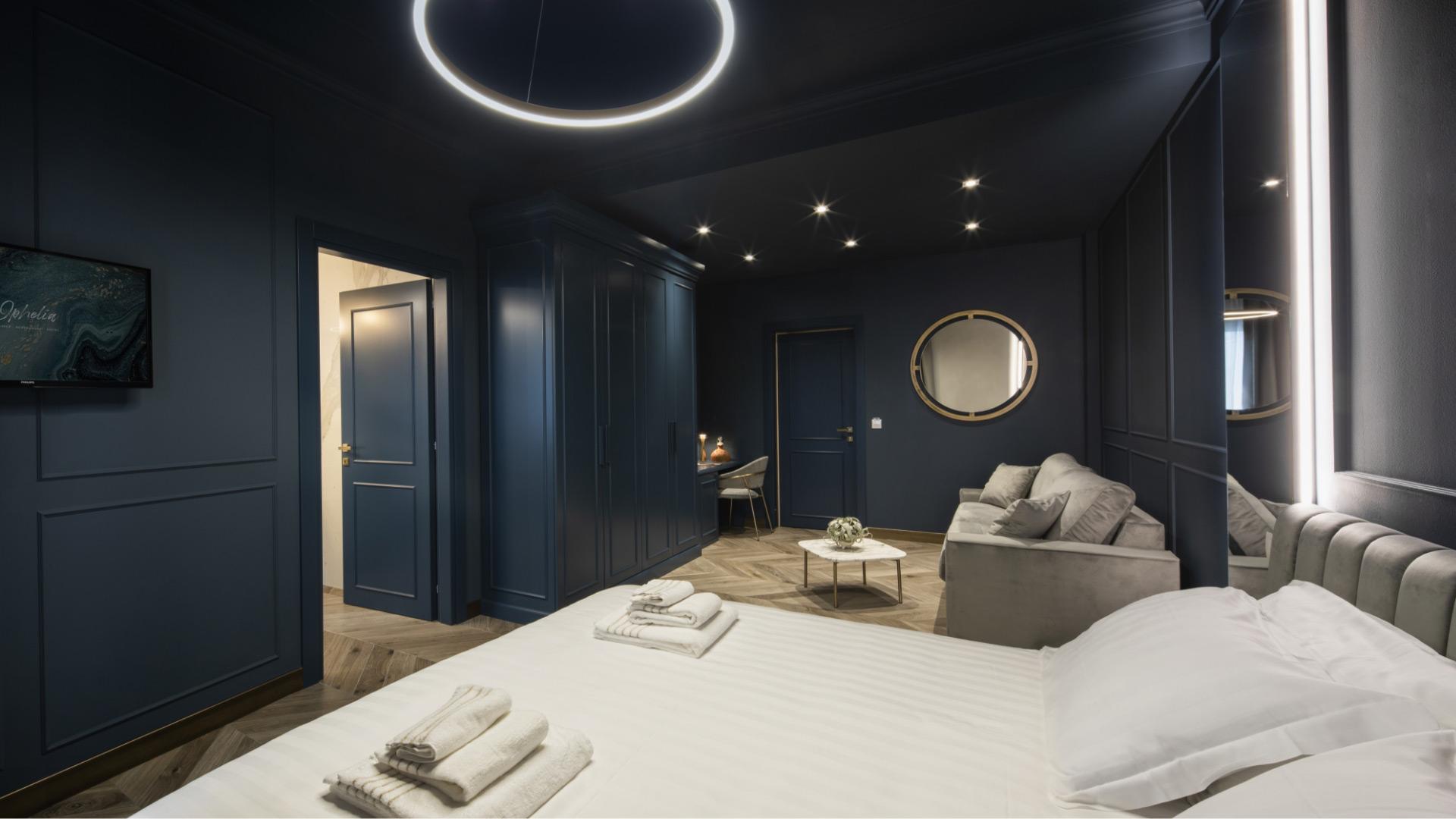 Camera moderna con pareti blu, letto, divano e illuminazione elegante.