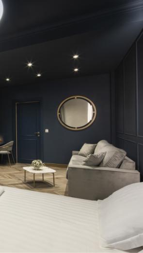 Camera moderna con pareti blu, letto, divano e illuminazione elegante.