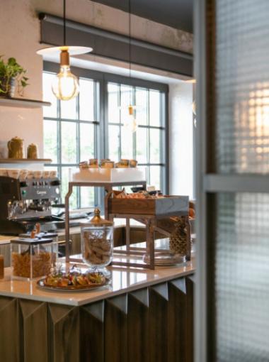 Cozy café corner with pastries, coffee machine, and warm lighting.