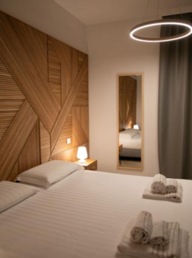 Modern bedroom with wooden wall design, cozy lighting, and neatly arranged towels on the bed.