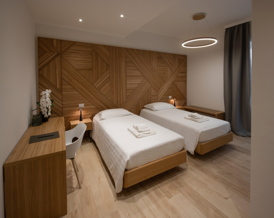 Modern room with twin beds, wooden decor, desk, and stylish lighting.