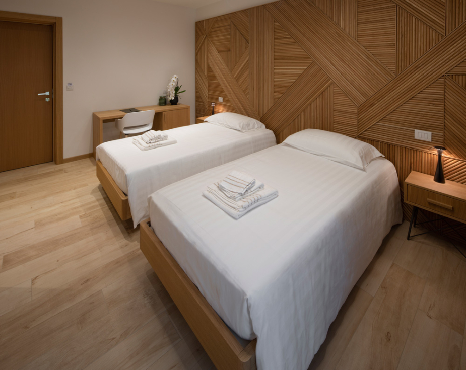 Modern twin bedroom with wood accents and minimalist design, featuring a circular ceiling light.