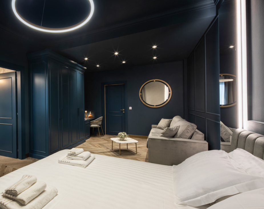 Elegant hotel room with dark blue walls, modern decor, and cozy seating area.