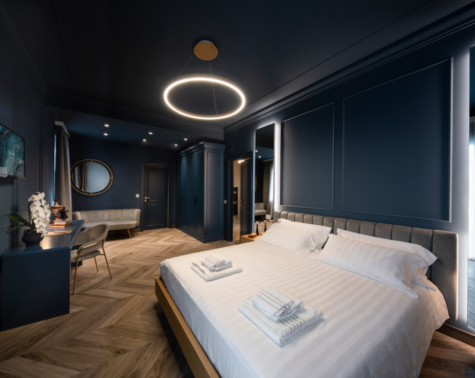 Elegant bedroom with dark blue walls, modern lighting, and wooden herringbone flooring.