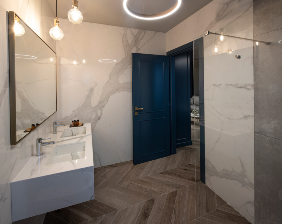 Modern bathroom with marble walls, wooden floors, and elegant lighting fixtures.