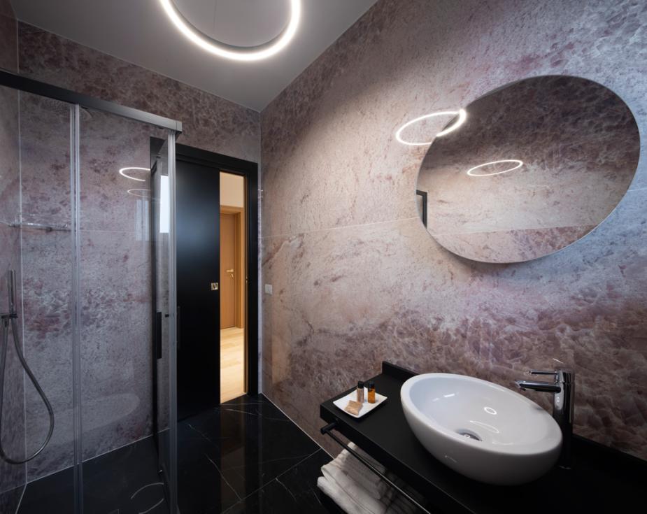 Modern bathroom with shower, oval mirror, and sleek sink on a black countertop.