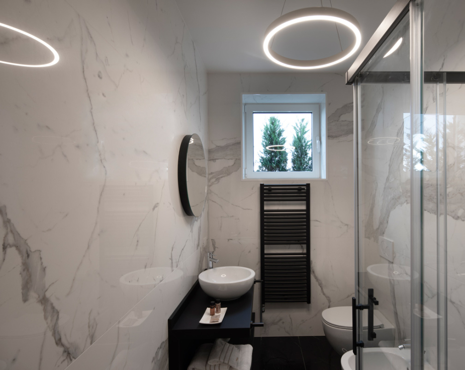 Modern bathroom with marble walls, circular mirror, and sleek fixtures.