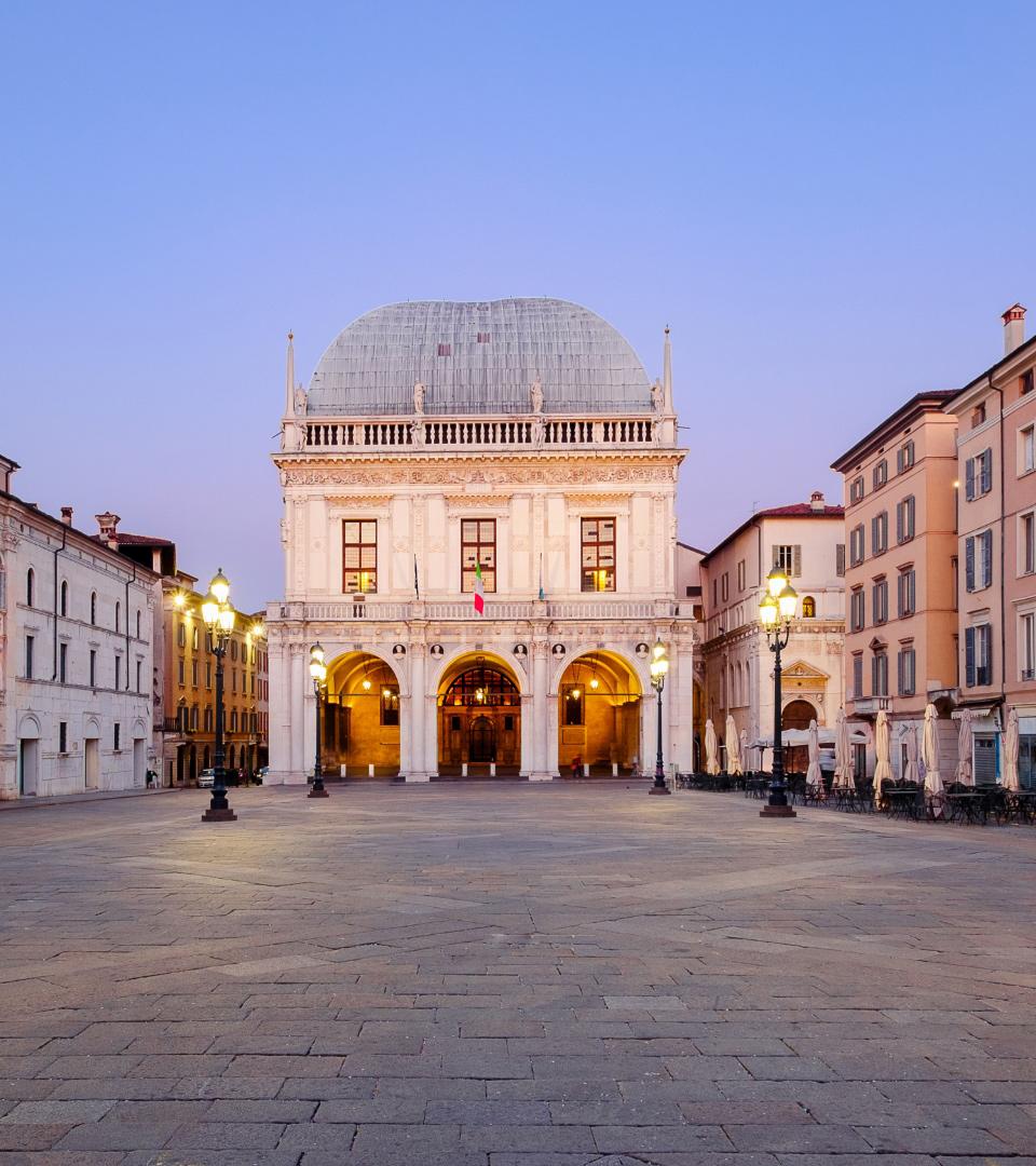 Historic building in an open square, illuminated by street lamps at dusk.